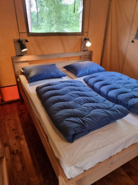 Gemütliches Bett mit blauer Bettwäsche im Safari-Zelt mit Bad auf Camping het Horstmannsbos, Niederlande.