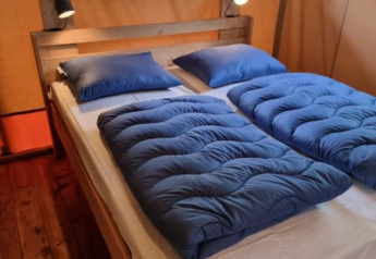 Letto accogliente con biancheria blu nella tenda Safari con bagno al Camping het Horstmannsbos, Olanda.