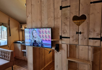 Interno di tenda safari con pareti in legno, TV a muro e intaglio a cuore, Camping het Horstmannsbos.