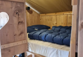 Ingresso a letto accogliente con coperte blu in una tenda safari di legno nei Paesi Bassi.