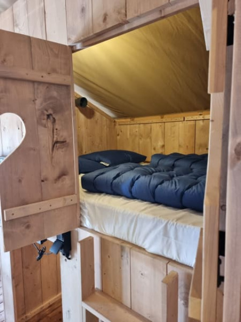 Eingang zu einem gemütlichen Schlafbereich mit Holzwänden und blauer Bettdecke in einem Safarizelt.