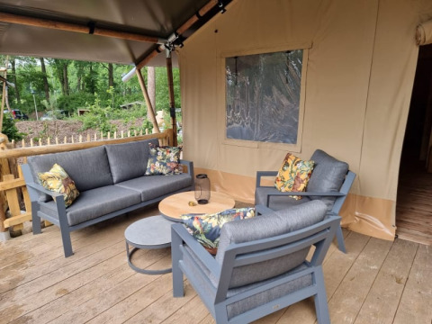 Outdoor seating area with gray furniture and floral cushions in front of a safari tent at Camping het Horstmannsbos.