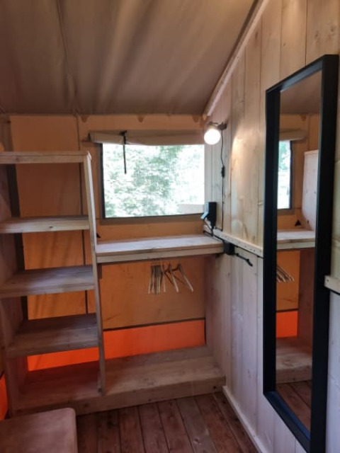 Interior view of Safari tent at Camping het Horstmannsbos, Netherlands, with wooden shelves, mirror, and window.