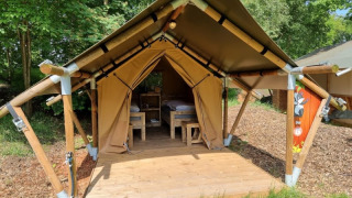 Safari tent named Duolodge with wooden deck and beds, set on a campsite surrounded by green trees.