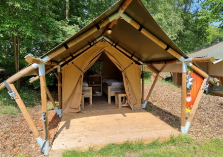 Safaritent genaamd Duolodge met houten veranda en bedden, gelegen op een camping tussen groene bomen.