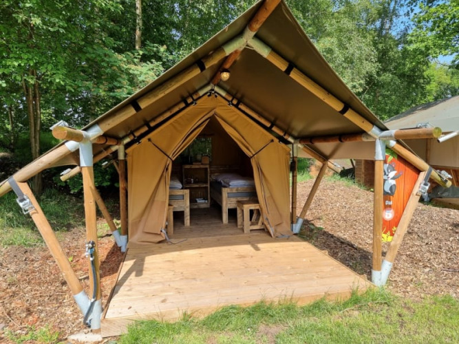 Tienda safari llamada Duolodge con terraza de madera y camas, situada en un camping rodeado de árboles.