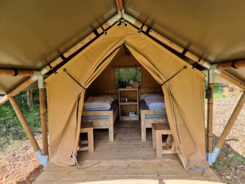 The inside of a safari tent with two beds and wooden furniture at Camping het Horstmannsbos in the Netherlands.