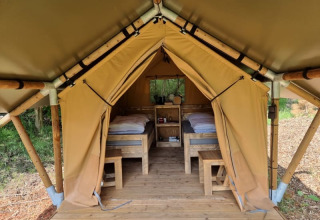 The inside of a safari tent with two beds and wooden furniture at Camping het Horstmannsbos in the Netherlands.