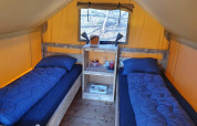Interior de una tienda safari Duolodge con dos camas individuales y ropa de cama azul en Camping het Horstmannsbos, Países Bajos.