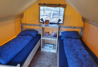 Interior de una tienda safari Duolodge con dos camas individuales y ropa de cama azul en Camping het Horstmannsbos, Países Bajos.