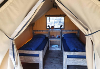Interior of a safari tent with two single beds and wooden furniture at Camping het Horstmannsbos, Netherlands.
