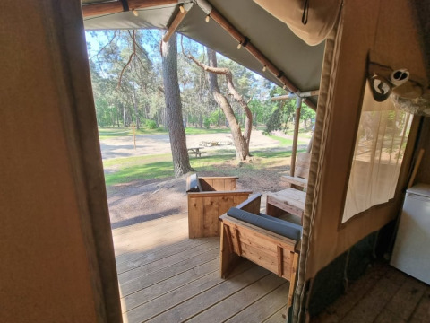 Vista dal patio di una tenda safari con mobili in legno al Camping het Horstmannsbos, Paesi Bassi, tra alberi.