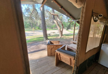 Udsigt fra en safaritelts veranda med træmøbler i Camping het Horstmannsbos, Holland, mod grønne træer.