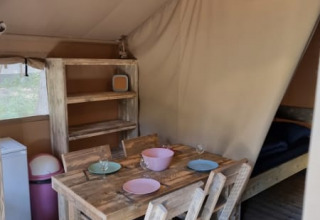 Interior of Safari tent with rustic wooden dining table, chairs, shelf, soft lighting, and cozy decor.