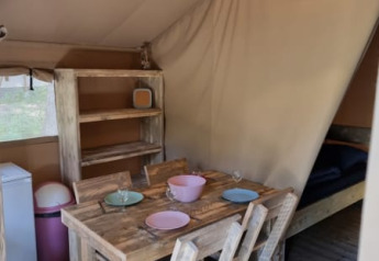 Innenansicht eines Safari-Zelts mit rustikalen Holzmöbeln, Esstisch, Stühlen und Regal.