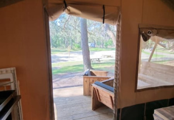 Indvendigt udsyn fra en safariteltsdør på Camping het Horstmannsbos, Holland, med træveranda udenfor.