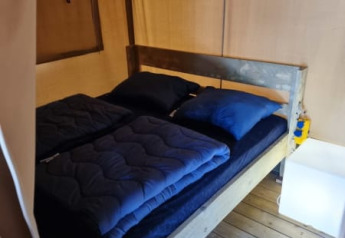 Vista interior de una tienda safari con cama doble en Camping het Horstmannsbos, Países Bajos.