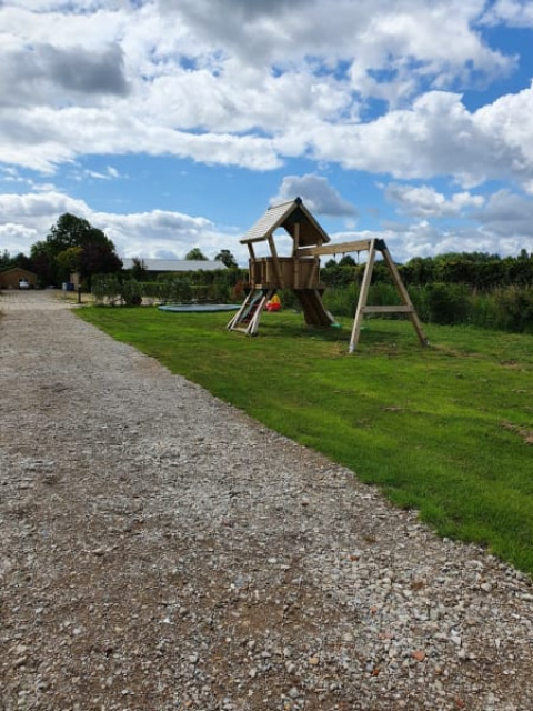 Spielplatz und Kiesweg am Safari-Zelt auf Camping de Oude Rijn in den Niederlanden unter wolkigem Himmel.