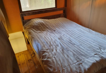 Vista interna di una tenda safari al Camping Elbeling in Germania, con letto accogliente e pavimento in legno.