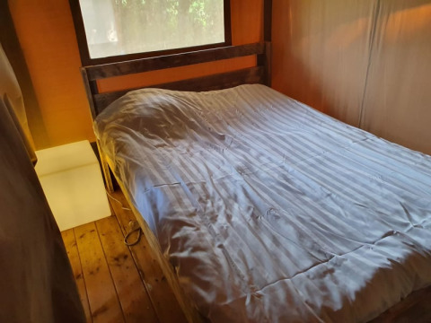 Vista interior de una tienda safari en Camping Elbeling, Alemania, con una cómoda cama y suelo de madera.