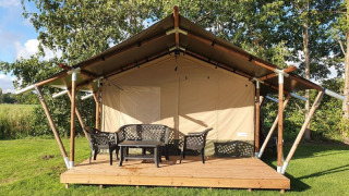 Tienda safari en Camping de Oude Rijn, Países Bajos, con terraza de madera y muebles de exterior verdes.