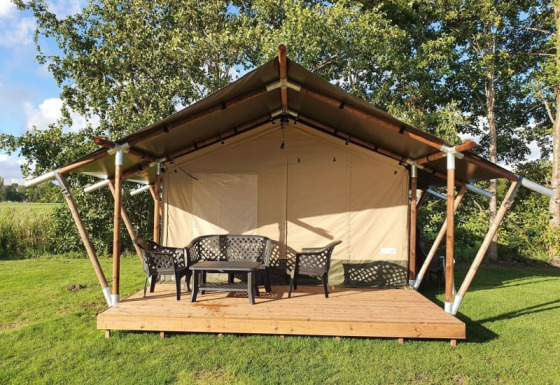 Tienda safari en Camping de Oude Rijn, Países Bajos, con terraza de madera y muebles de exterior verdes.