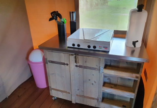 Cocina compacta en tienda safari en Camping la Cour d'Enchère, Francia, con encimera y utensilios.