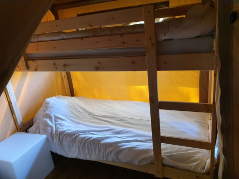 Ein gemütliches Zimmer im Safarizelt mit Holz-Etagenbett und warmem, gelbem Zelthintergrund.