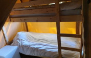 Acogedor dormitorio dentro de una tienda safari con literas de madera y luz cálida amarilla.