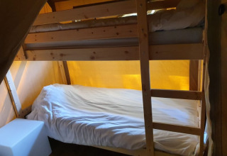 Acogedor dormitorio dentro de una tienda safari con literas de madera y luz cálida amarilla.