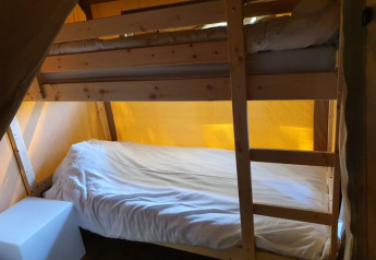 Et hyggeligt værelse i en safari-telt med køjesenge i træramme og varmt, gult teltlys omkring.