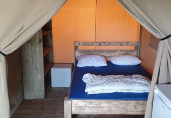 Vista interna di una tenda safari con pavimento in legno, letto matrimoniale, scaffali e frigorifero.