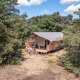 Safari telt midt i skoven med familie på terrassen, omgivet af træer under en blå himmel.