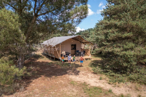Familia disfruta al aire libre junto a una tienda safari en Camping GT Keiheuvel, rodeada de bosque en Bélgica.