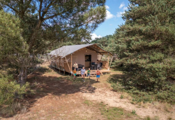 Famiglia si gode la natura davanti a una tenda safari al Camping GT Keiheuvel circondata da bosco in Belgio.