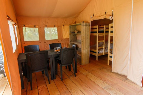 Interno di tenda Safari con tavolo da pranzo, sedie di plastica e letti a castello su pavimento in legno.