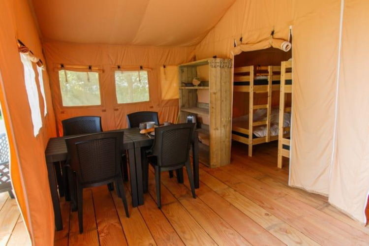 Binnenkant van Safari tent met eettafel, plastic stoelen en stapelbedden op houten vloer.