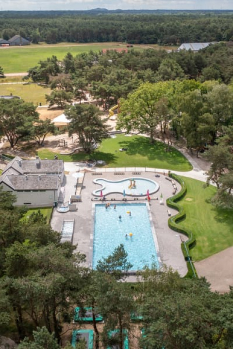 Vista aérea de una piscina y zona de juegos rodeada de árboles en la tienda Safari en Camping GT Keiheuvel, Bélgica.