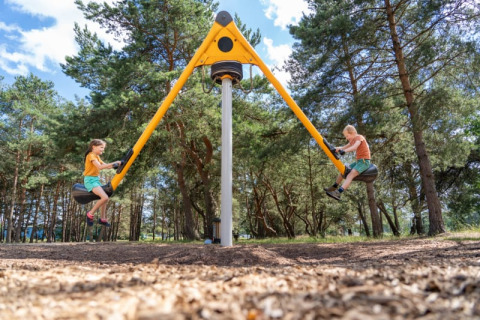 Dos niños juegan en un columpio moderno en la zona de tienda safari de Camping GT Keiheuvel, Bélgica.