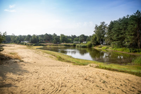 Vista del lago y la playa de arena en la Safari tent de Camping GT Keiheuvel en Bélgica, rodeada de árboles.