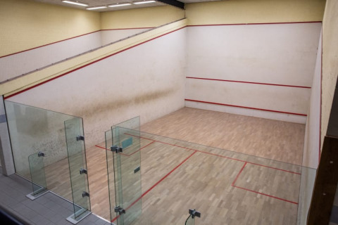 Cancha de squash interior con suelo de madera, paredes de vidrio y líneas rojas de demarcación.