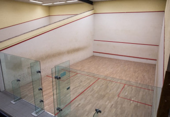 Campo da squash al coperto con pavimento in legno, pareti di vetro e linee rosse evidenti.