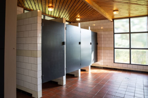 Baño público moderno con puertas de cabina negras, azulejos blancos y grandes ventanales en Camping GT Keiheuvel.