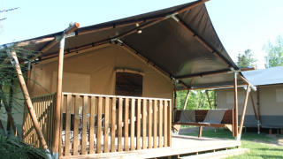 Tenda safari con veranda privata e servizi igienici, immersa nel verde per un'esperienza glamping.