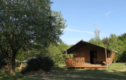 Safari telt med egen veranda og bad ved Tolne Camping, Danmark, omgivet af grønne træer under blå himmel.