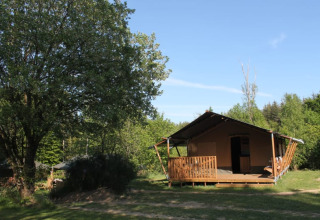 Tente safari avec terrasse et sanitaires privés au Tolne Camping au Danemark, entourée de verdure et d’arbres.