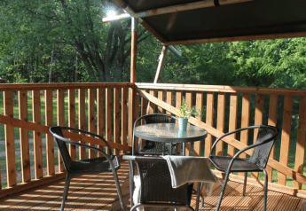 Terrazza in legno soleggiata con tavolo e sedie al Safari tent + servizi igienici a Tolne Camping, Danimarca.