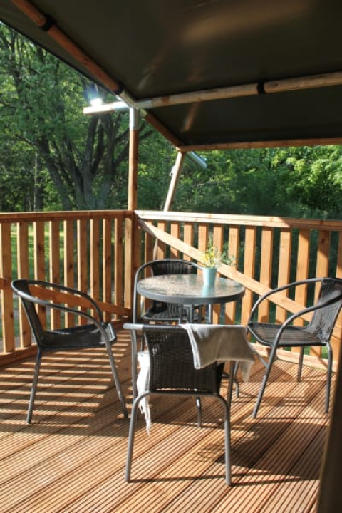 Terraza cubierta con mesa y sillas en la tienda Safari con sanitario en Tolne Camping, Dinamarca, con vista verde.