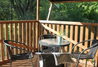 Terraza cubierta con mesa y sillas en la tienda Safari con sanitario en Tolne Camping, Dinamarca, con vista verde.