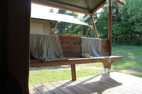 Vista desde una tienda safari con terraza y banco de madera en Tolne Camping, Dinamarca, rodeado de naturaleza.
